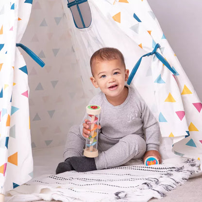A baby sitting in a teepee with a Bigjigs Garden Rainmaker inside.