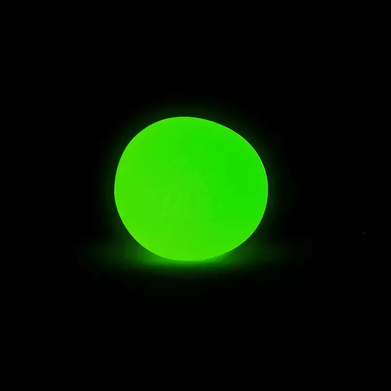 A vibrant neon green Glow in the Dark Needoh circle glowing brightly against a dark black background, creating a stark and visually striking contrast.