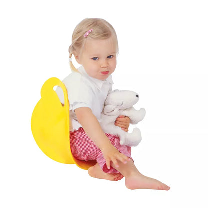 A toddler with a pink hair clip holding a plush toy and a Spinner Blue while sitting on a yellow potty chair, looking thoughtfully to the side.