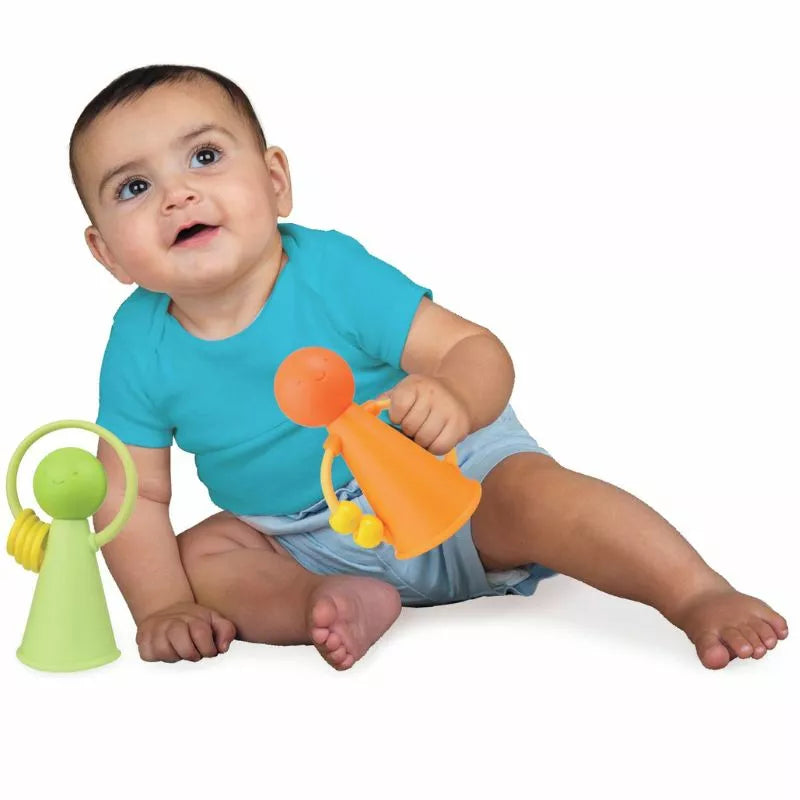 A curious baby sitting on the floor, holding a Halilit Music Pals Duet Green and Orange toy, and looking up with a look of wonder and amusement.