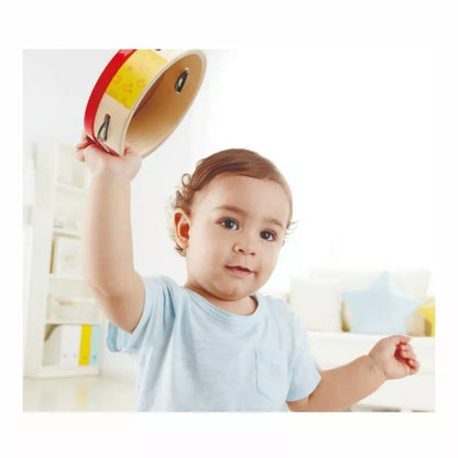 A young child is holding a Hape Tap-along Tambourine in the air.