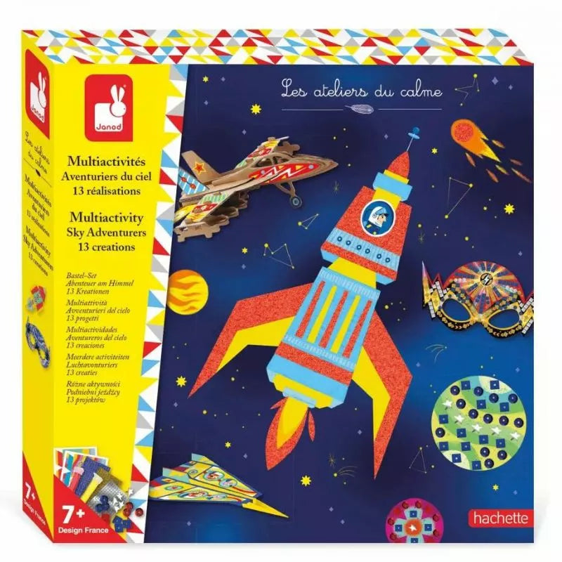 The image shows a colorful activity kit box labeled "Janod Multiactivity Sky Adventurers" by Janod, containing 13 hands-on craft activities for kids aged 7 and up. The box features illustrated rockets, airplanes, and stars on a dark blue background, perfect for sky and space-themed fun.