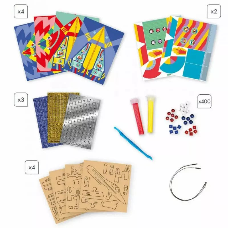 A variety of craft materials are displayed, perfect for hands-on craft activities. The Janod Multiactivity Sky Adventurers kit includes colorful patterned paper sheets with rocket designs (x4), circular patterns (x2), metallic sticker sheets (x3), test tubes with liquids, small cubes (x400), stencil sheets (x4), a blue plastic tool, and a wire.