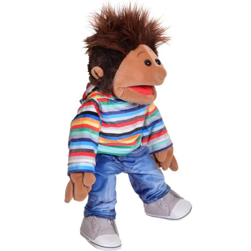 The Johann Boy Hand Puppet - 45cm features brown skin, spiky brown hair, a colorful striped hoodie, blue jeans, and gray sneakers. Its mouth is open and hands are positioned in front.