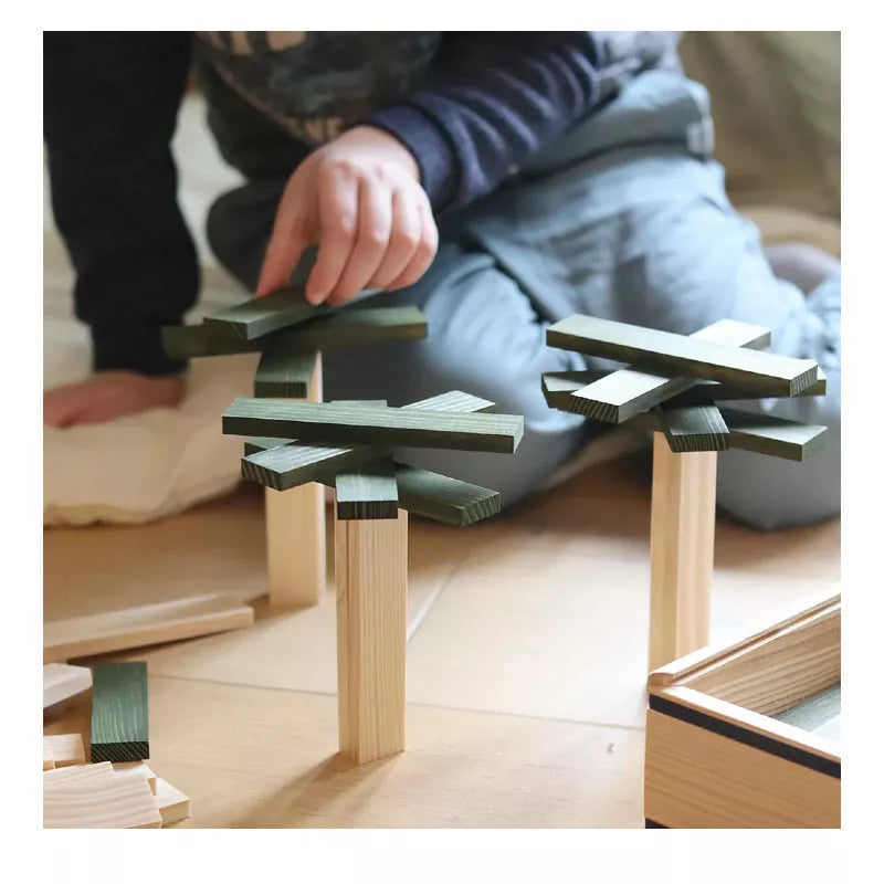 A child playing with KAPLA® 40 Coloured Planks Green on the floor.