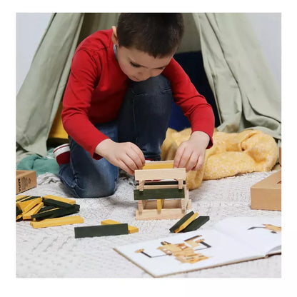 A young boy playing with KAPLA® 40 Coloured Planks (Green & Yellow) and Book toy.