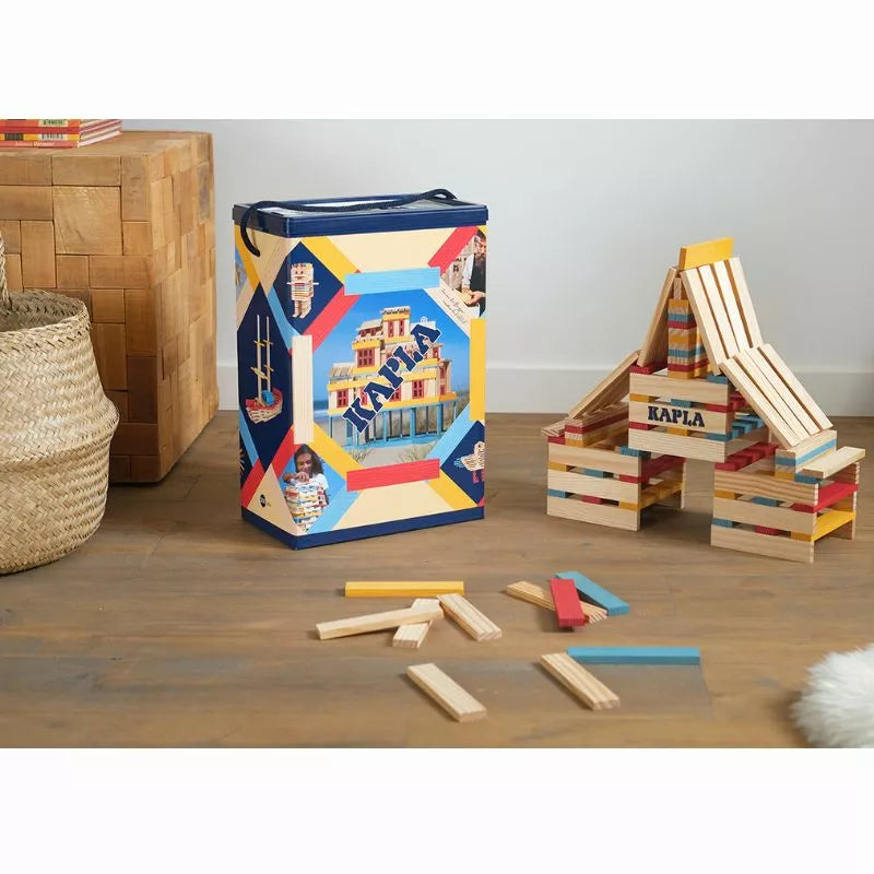 A vibrant and colorful children's playroom with a creatively designed KAPLA® 200 Summer Box featuring a nautical theme, surrounded by Kapla planks and a mini wooden chair, all atop a hardwood floor against a neutral
