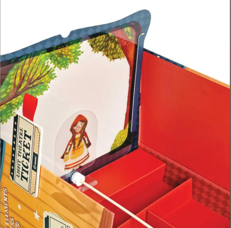 An open Shadow Theatre – The Amazing Light Theatre of Wonders box reveals a pop-up girl in a red hood among trees, with red and orange compartments and ticket illustration—perfect for imaginative play or your own light theatre.
