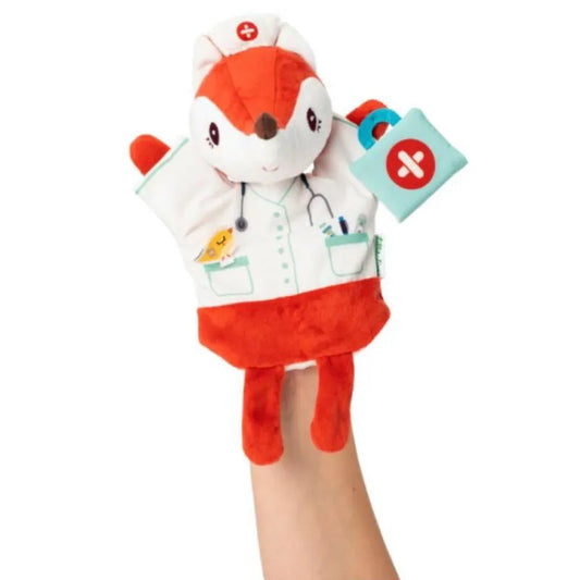 The Lilliputiens Alice Doctor Handpuppet, a plush fox dressed as a nurse with a red cross hat and white coat, is being held up by a hand. This hand puppet features detailed design elements like an embroidered stethoscope and medical tools on its coat, along with a small first aid kit in its right paw, making it perfect for imaginative play.