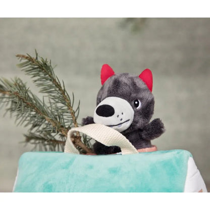 The Lilliputiens Houses Of The Wolf And The 3 Little Pigs set features a cute gray wolf puppet with red ears peeking from a teal and white bag, encouraging creative play and fine motor skill development, with a pine branch in the background.