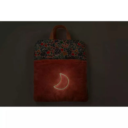 A dimly lit image showcasing a Lilliputiens Stella Bed Time Ritual with a colorful floral pattern at the top and a crescent moon design glowing on its lower suede-like textured section, perfect for children's bedtime adventures.