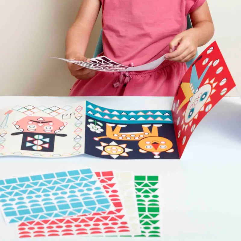 A child in a pink dress enjoys the Poppik Sticker Panorama – Circus, placing vibrant stickers on animal-themed art sheets and a panoramic poster. This creative kit features fun circus patterns, animals, and colorful sticker activities for kids.