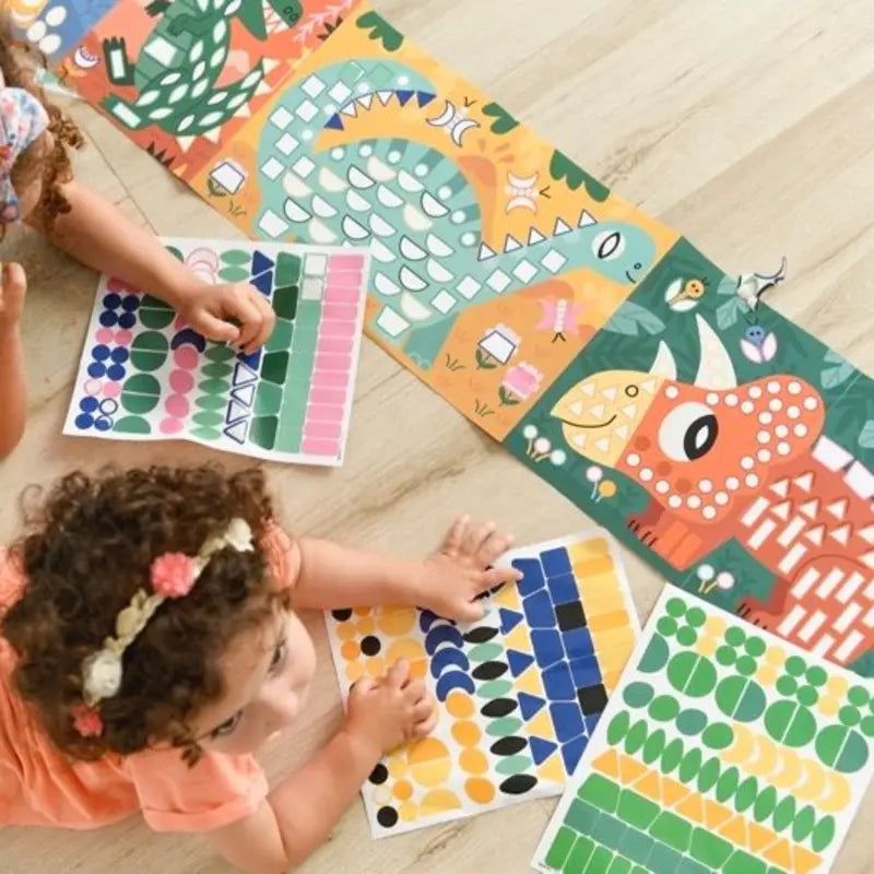 Two young children add stickers to a Poppik Sticker Panorama – Dinosaurs poster as part of a dinosaur-themed mosaic art project on a light wooden floor.