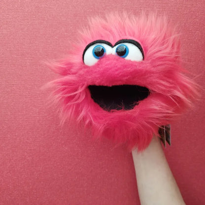 A Living Puppets Twaddle Hand Puppet, featuring a pink, furry monster with large blue eyes and a wide open mouth, is being held up against a pink background. The puppet, perfect for creative play, has a friendly and cheerful expression.