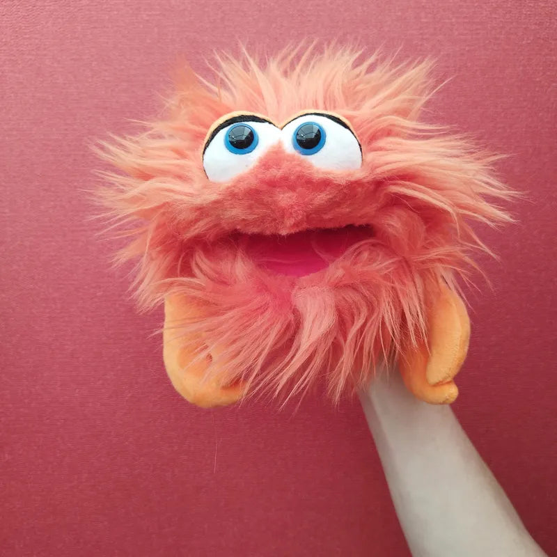 The Living Puppets Monster Hand Puppet Knipser, featuring bright orange, furry fabric and wide googly eyes, is displayed against a pink background. This delightful puppet boasts an open mouth and charming orange felt hands.