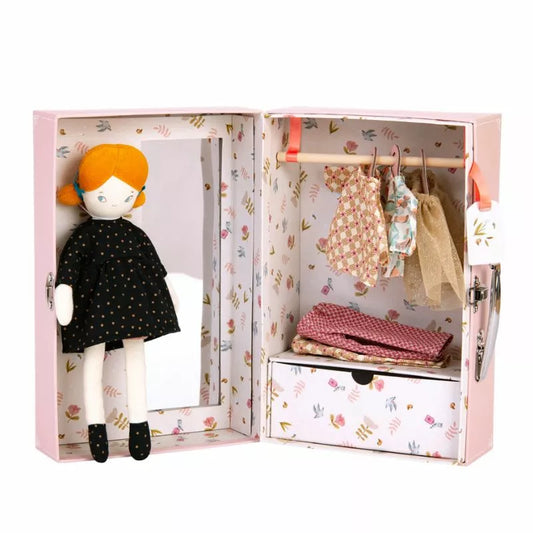 A Moulin Roty The Little Wardrobe Suitcase in a dollhouse with clothes hanging on a rack.