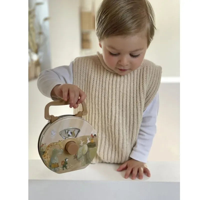 A young child in a cream sweater vest holds the Musical Radio Noah's Ark, which features charming animal illustrations reminiscent of a classic toy lunchbox. They are looking down and leaning slightly on a white surface, with the softly blurred background enhancing the nostalgic feel.