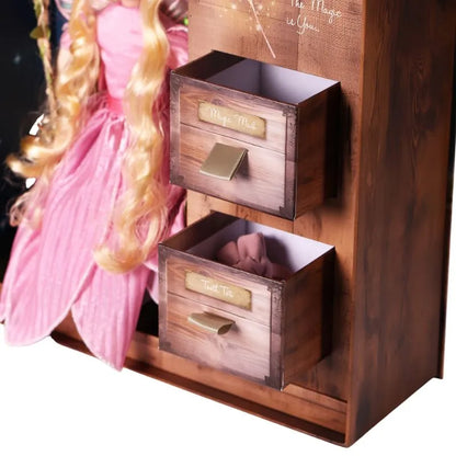 The My Forever Tooth Fairy Gift Set includes a charming wooden storage unit with two small drawers labeled "Magic Mail" and "Troll Toll." Additionally, a doll wearing a pink dress with long blonde hair is partially visible to the left of the unit, sparking children's imagination to fill this keepsake Tooth Fairy Gift Box.