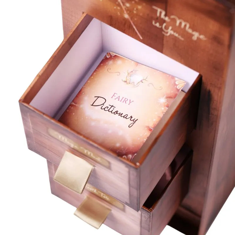 A small decorative "My Forever Tooth Fairy Gift Set" with gold ribbons partially open, revealing a book titled "Fairy Dictionary" inside. The box has a wood-like finish and the words "The Magic is You" inscribed in gold script on the inside of the lid, making it an enchanting keepsake that sparks children's imagination.