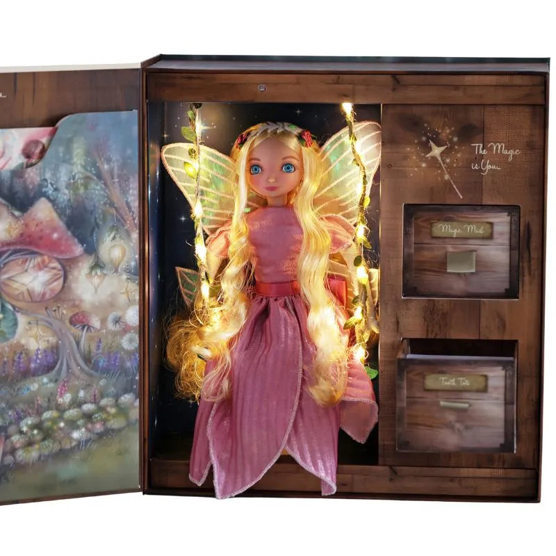 A fairy doll with long blonde hair, wearing a pink dress with yellow wings, is displayed in an open wooden box. The My Forever Tooth Fairy Gift Set features compartments labeled "Magic Wand" and "Fairy Tale," with one compartment containing twinkling fairy lights.