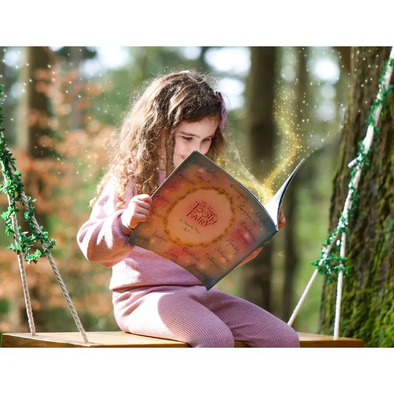 A young girl with curly hair, dressed in a pink outfit, sits on a wooden swing in a forest. She is intently reading "My Forever Tooth Fairy Gift Set," which emits a magical, glowing light. The background features blurred greenery and trees, creating magical memories that ignite children's imagination.