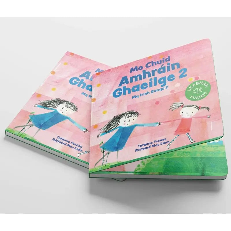 Two copies of "Mo Chuid Amhráin Ghaeilge 2" are stacked, showing playful drawings of two girls holding hands on a pink and green cover—an ideal book for introducing Irish songs to children.