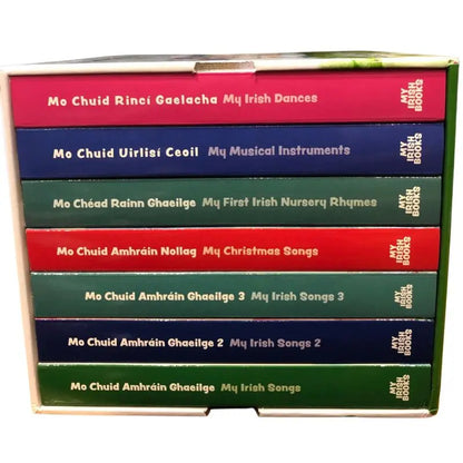 The My Irish Books Bailiúcháin 7 Books set features seven colorful children’s books, each labeled in Irish and English, with titles like "My Irish Dances," "My Musical Instruments," and "My Christmas Songs," all neatly boxed upright.