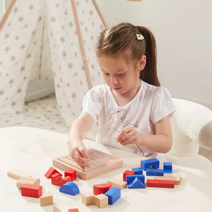 A young girl is playing with the 3D Block Building Game, enhancing her spatial awareness by placing colorful wooden geometric shapes on a grid board at a table. In the background, a teepee tent with a star pattern adorns the bright and airy playroom, creating a clean and well-lit environment.