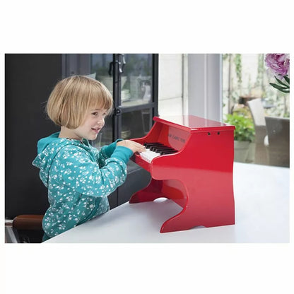 A little girl playing a New Classic Toys Red Piano 18 keys in a room.