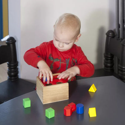 A young child playing with the New Classic Toys Shape Sorting Cube on a table.