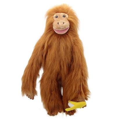 The Puppet Company Large Puppet Orangutan, featuring long brown fur and a smiling face, holds a small yellow banana in one hand. This plush primate toy is perfect for imaginative play and stands upright against a plain white background.