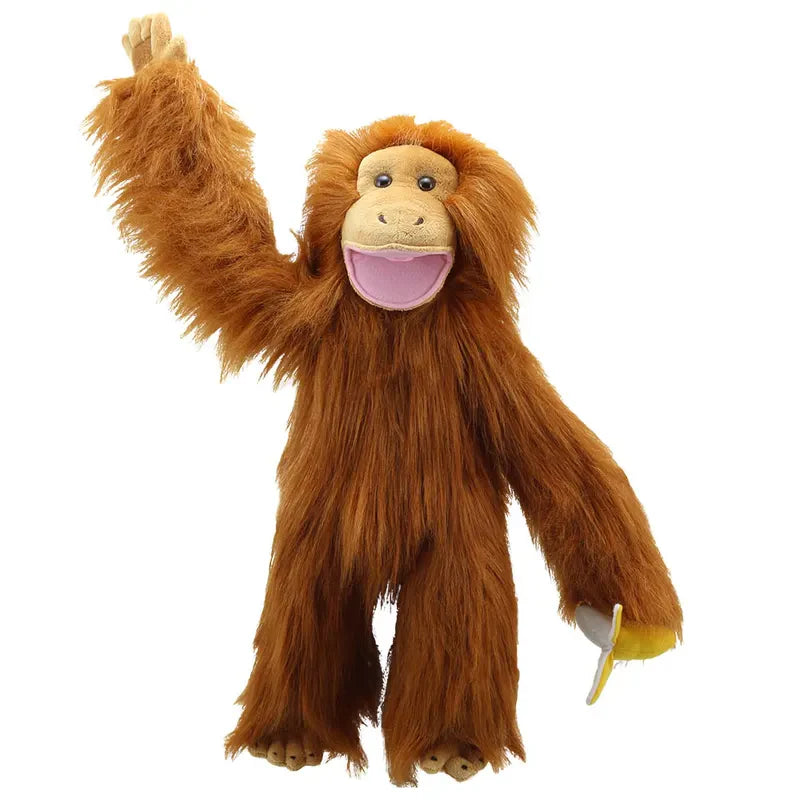 The Puppet Company Medium Puppet Primate Orangutan is a plush monkey puppet with long orange fur, a wide pink mouth, one arm raised as if waving, and a movable mouth for lifelike play. It holds a peeled banana in its other hand.