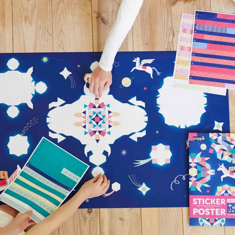 Two people place repositionable stickers onto the vibrant Poppik Creative Sticker Poster – Constellation. Sticker sheets and the "Sticker Poster" box are scattered on the floor around the geometric mosaic pixel art poster.