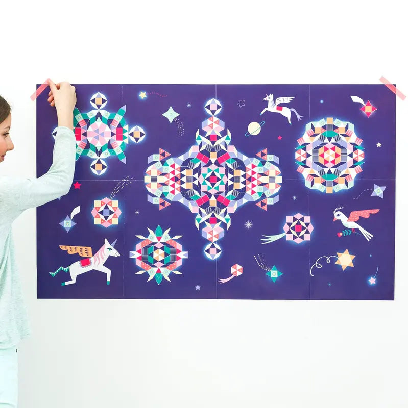 A person holds a Poppik Creative Sticker Poster – Constellation against a purple wall, showing a large unicorn, geometric patterns, stars, and pastel mythical creatures in a colorful mosaic design.