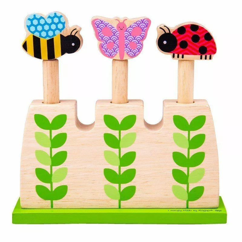 A Garden Pop up Toy featuring three pegs, each topped with a colorful insect: a blue bee, a pink butterfly, and a red ladybug, all mounted on green plant stalks.