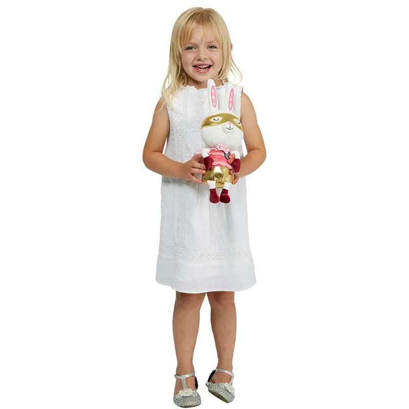 A young girl with blonde hair, wearing a white dress, smiles while holding a Wilberry Super Hero Rabbit dressed in a colorful outfit with a mask. The imaginative play comes to life as she stands against a plain white background.