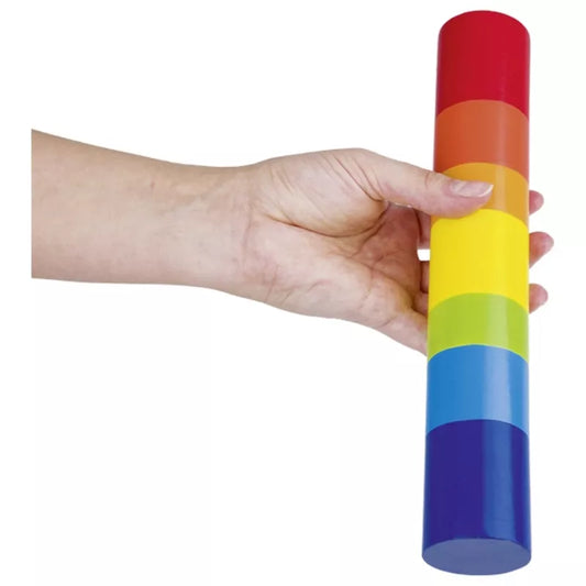 A hand holds the Goki Rain Stick, a cylindrical sensory toy featuring colorful stacked segments in a rainbow pattern.