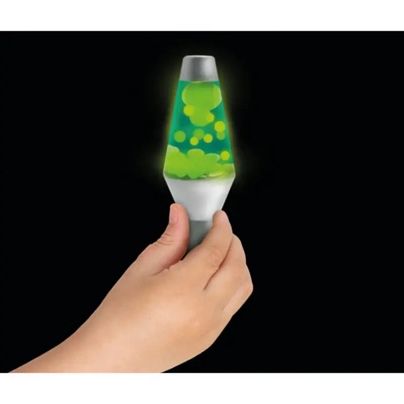 A hand holds a Lava Squish N Flow Needoh with a silver base and cap, filled with glowing green liquid and blobs, against a black background—a mesmerizing glow-in-the-dark fidget toy.