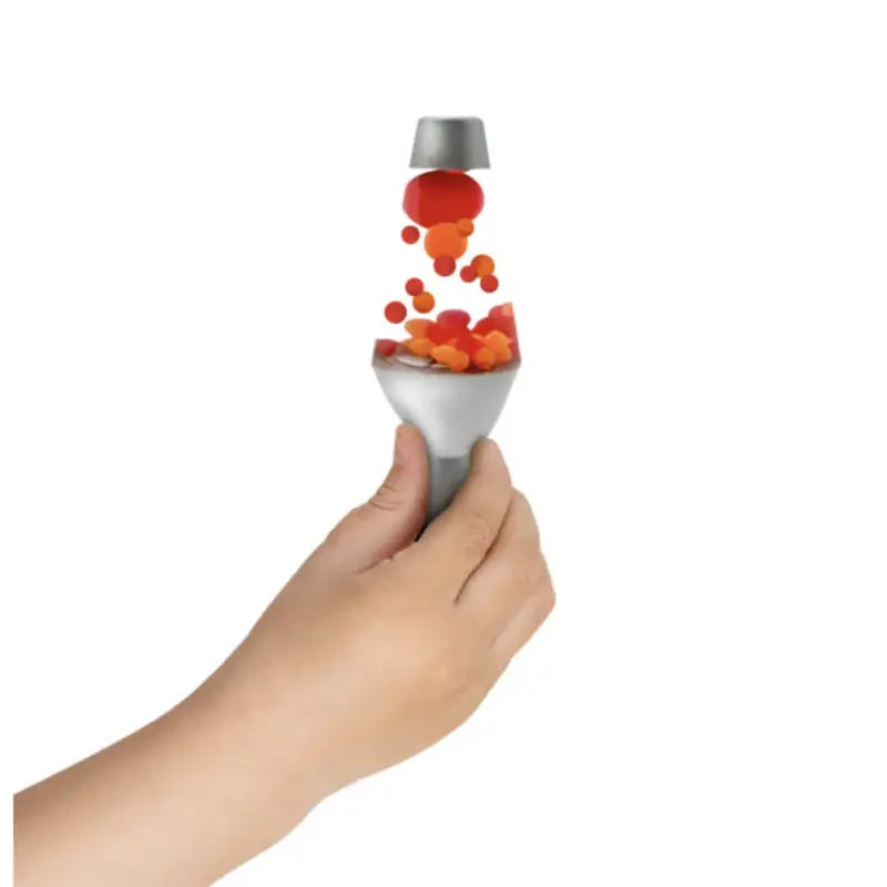 A hand holds the Lava Squish N Flow Needoh—a silver object, split in two, with red and orange blobs flowing mesmerically between the halves like a mini lava lamp.