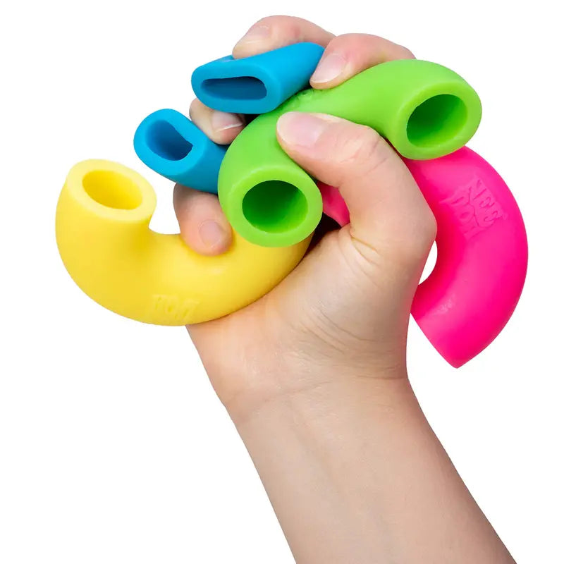 A hand grips four Mac and Squeeze Needoh noodles—yellow, blue, green, and pink—each curved and hollow, against a white background. These colorful tubes are perfect stress relief toys for anyone who loves tactile play.