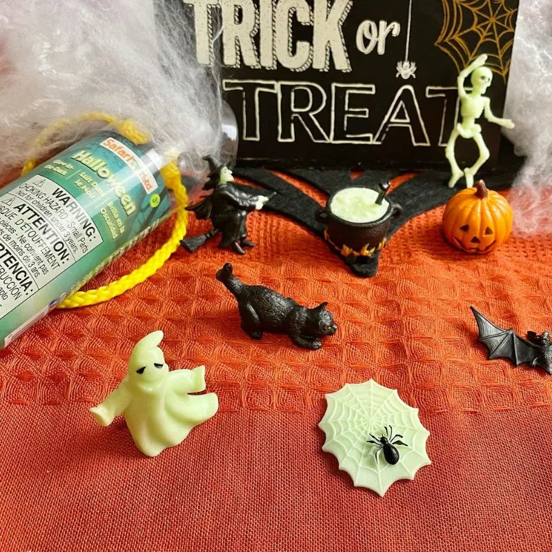 Halloween-themed display featuring a small ghost and black cat TOOBS® Figurines Halloween Glow in the Dark, a rubber bat, spider, pumpkin, a tube of face paint, and a "trick or treat