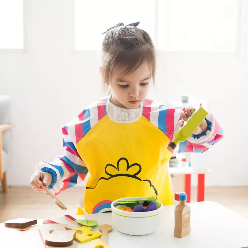 A little girl in a yellow bib is playing with her New Classic Toys Salad Set Pretend Playfood.