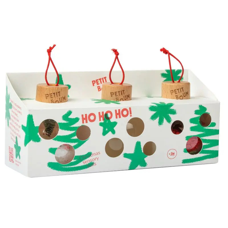 The Christmas Sensory Baubles come in a white box with green stars and "HO HO HO!" in red, featuring circular cutouts to display three baby-safe, unbreakable ornaments with red strings and "PETIT BAUM" engraved.