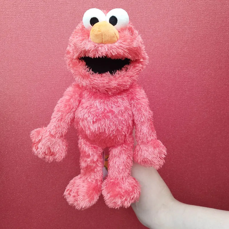 A hand displays the Living Puppets Elmo Sesame Street Hand Puppet against a red background. Elmo, the vibrant red character with large white eyes and an orange nose, is cherished for aiding children in developing social skills through playful interaction.