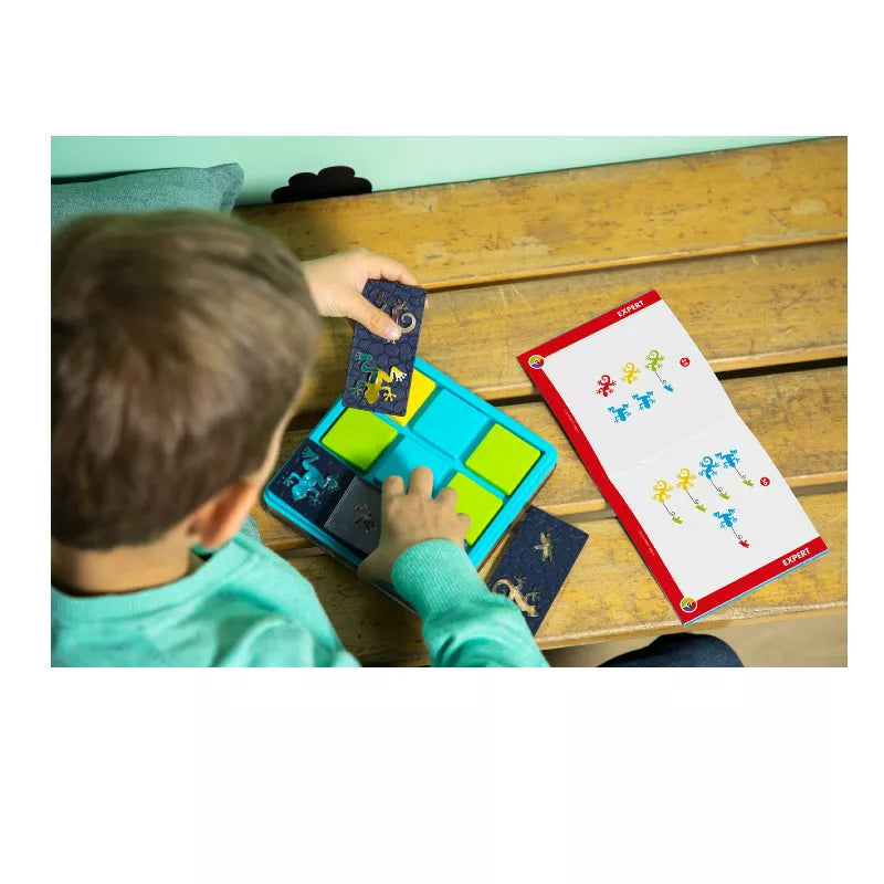 A young boy engaged in problem solving while playing with the SmartGames Colour Catch on a bench.