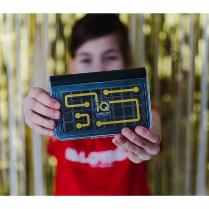 A girl is holding up a SmartGames IQ Circuit with a yellow and black design.