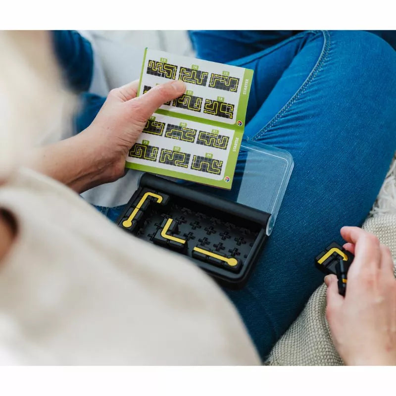 A woman is sitting on a bed with a SmartGames IQ Circuit in her hands, peacefully engrossed in her reading.