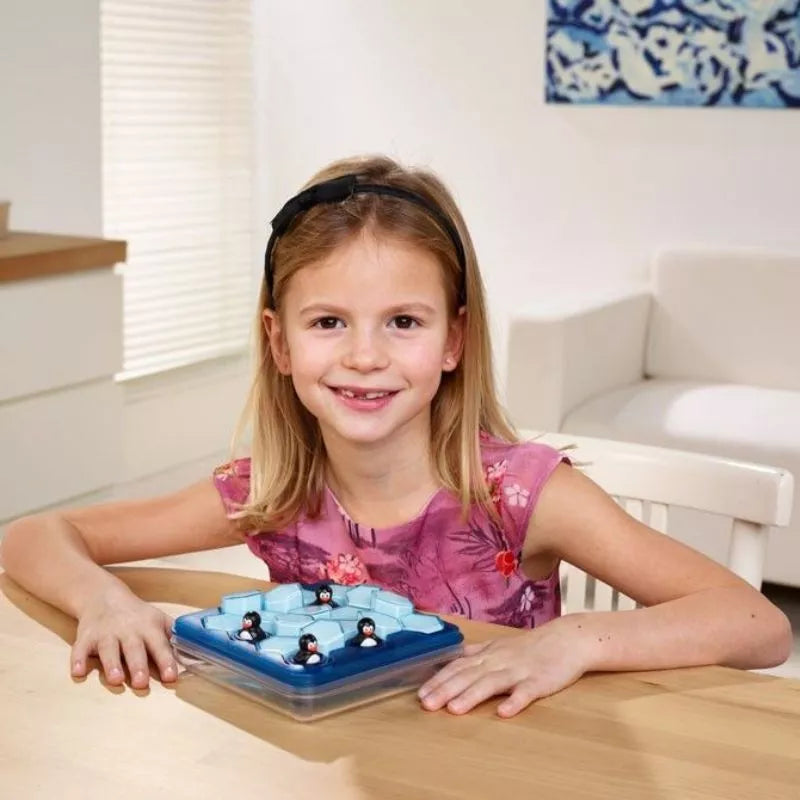 A little girl sitting at a table with a toy penguin from the SmartGames Penguins Pool Party.