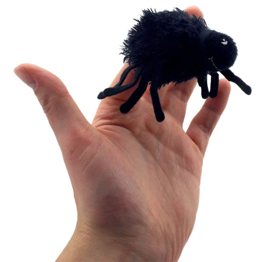 A hand is holding The Puppet Company Finger Puppet Spider Furry, a small, fuzzy black spider figurine with multiple legs that resembles a finger puppet. The spider rests on the fingers, its soft and fluffy texture making it ideal for storytelling against a plain white background.