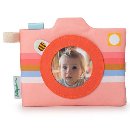 The Lilliputiens I'm Discovering Stella Photo Album is a soft, colorful fabric toy camera, ideal as a baby’s first gift. It features a circular photo frame for a baby's picture and comes with pink, orange, and white stripes plus playful details like a bee sticker.